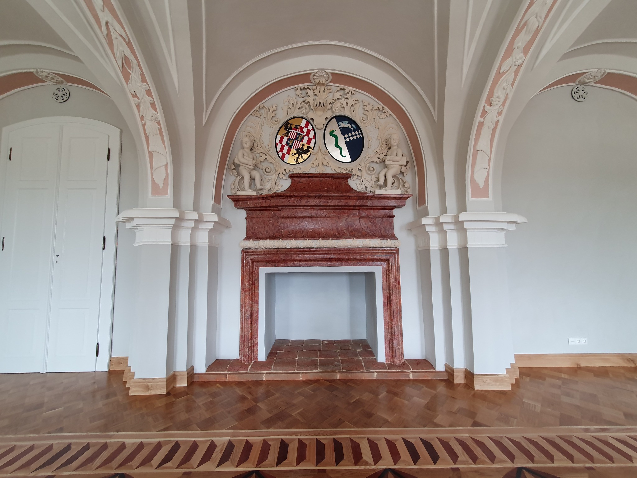 Stylowe wykończenie wnętrza w Świdnicy: dekoracyjny kominek z herbami, parkiet w jodełkę i łukowe sklepienia z ornamentami. Klasyczny design.
