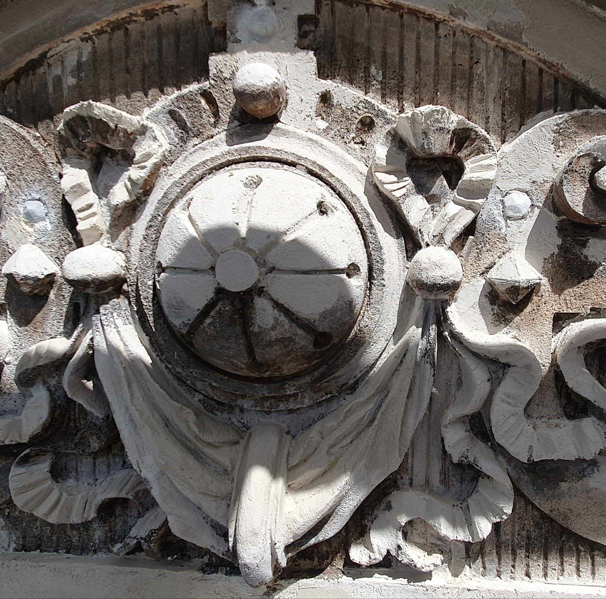 Detal fasady: dekoracyjny element architektoniczny z ornamentami roślinnymi i geometrycznymi, wykonany z jasnego kamienia, oświetlony bocznym światłem słonecznym.