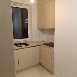 Wojciech Ulrych - Jasna kuchnia na wymiar z beżowymi frontami i kamiennym blatem, widok na zlew i płytę indukcyjną. Minimalistyczny design, nowoczesne wykończenie.