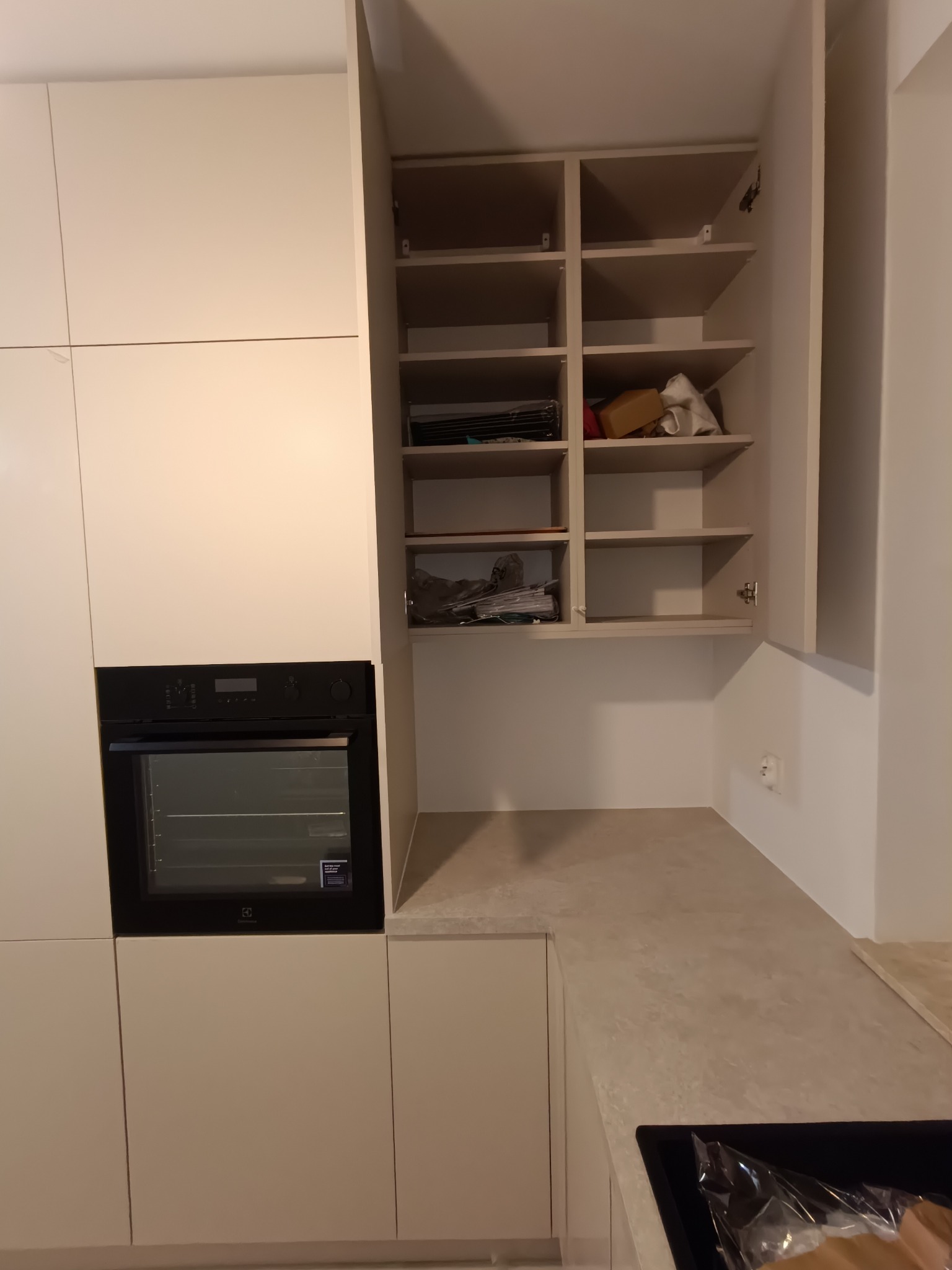 Jasna kuchnia na wymiar z zabudowaną piekarnikiem i otwartą szafką z półkami. Widoczne przedmioty wewnątrz szafki. Minimalistyczny design.