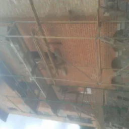 Wznoszenie muru z czerwonej cegły na rusztowaniu, widok z dołu na budynek w trakcie budowy.