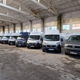 Thermotech - Flota firmowa: równe rzędy busów Thermotech i Drutex w hali magazynowej, gotowe do transportu okien i drzwi. Jasne światło podkreśla czystość i profesjonalizm.