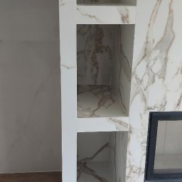 REMAR MARIUSZ GODLEWSKI - Wykończona wnęka z półkami, obłożona płytami imitującymi marmur, z widocznym fragmentem kominka. Nowoczesny design wnętrza.