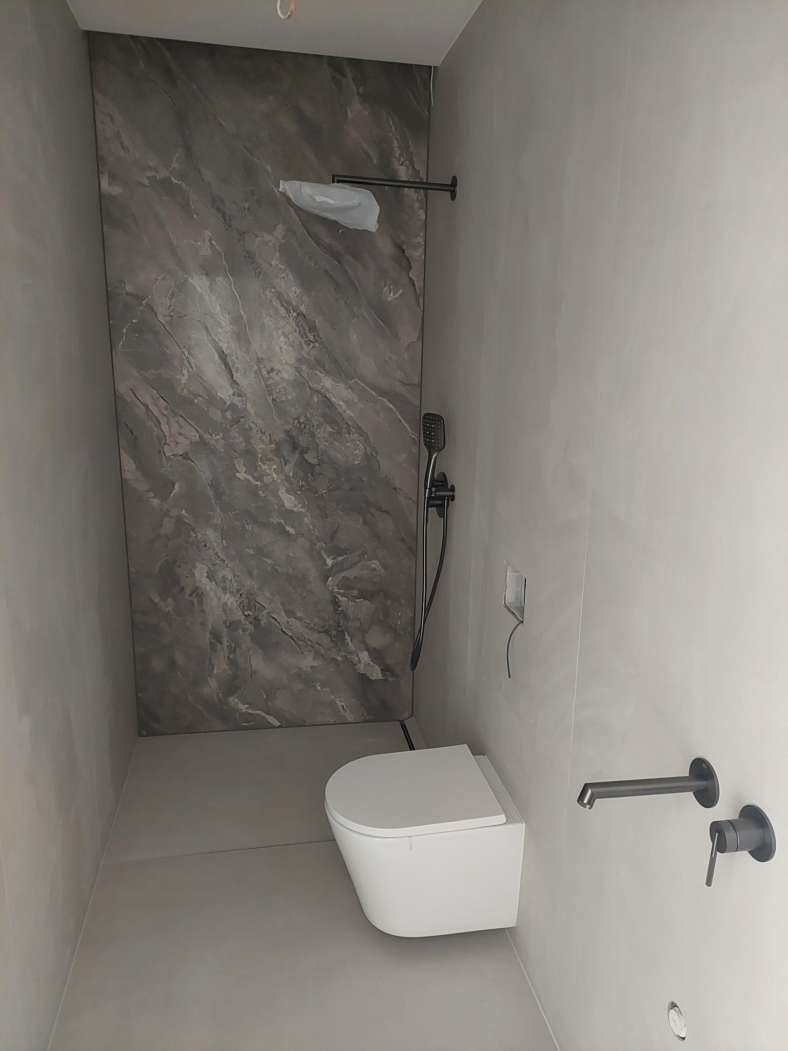 Nowoczesna łazienka z marmurową ścianą, podwieszaną toaletą i minimalistyczną armaturą w kolorze grafitowym. Świeżo wykończone wnętrze.