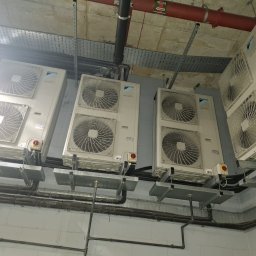 Mateusz Struzik MSAIR - Zamontowane jednostki zewnętrzne klimatyzacji Daikin na metalowych wspornikach, widoczne rury instalacyjne i elementy wentylacji pod sufitem w pomieszczeniu technicznym.