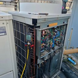 Mateusz Struzik MSAIR - Otwarta obudowa klimatyzatora na dachu z widocznymi przewodami, elektroniką i narzędziami pomiarowymi. Detaliczny widok na skomplikowaną instalację podczas serwisu.