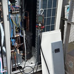 Mateusz Struzik MSAIR - Otwarta obudowa klimatyzatora z widocznymi elementami wewnętrznymi, w tym rurami miedzianymi, elektroniką i narzędziami diagnostycznymi. Widoczne panele obudowy obok urządzenia.