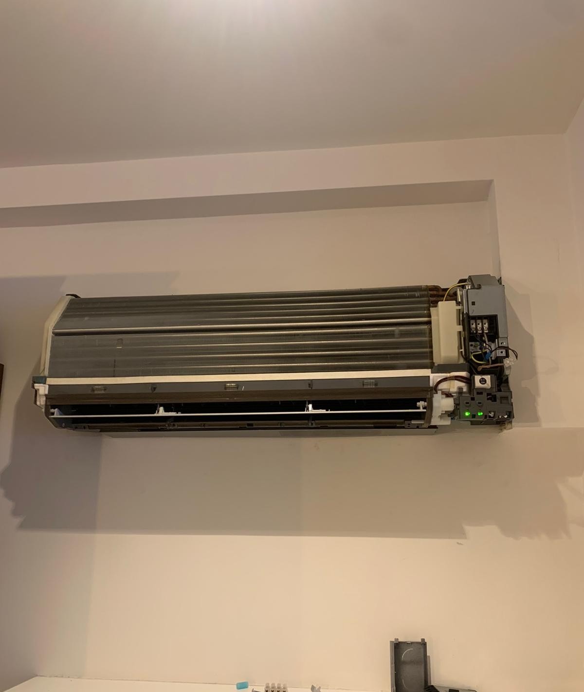 Ścienna jednostka klimatyzacji po zdjęciu obudowy, widoczne elementy wewnętrzne i podłączenia elektryczne. Urządzenie zamontowane na jasnej ścianie.