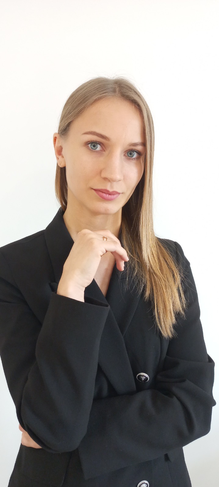 Portret kobiety w czarnej marynarce na białym tle, z ręką pod brodą i delikatnym uśmiechem, prezentujący profesjonalny wizerunek.