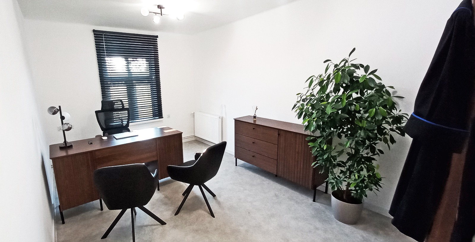 Nowoczesne biuro prawnicze z drewnianymi meblami, rośliną doniczkową i togą adwokacką wiszącą na ścianie. Minimalistyczny design, stonowana kolorystyka.