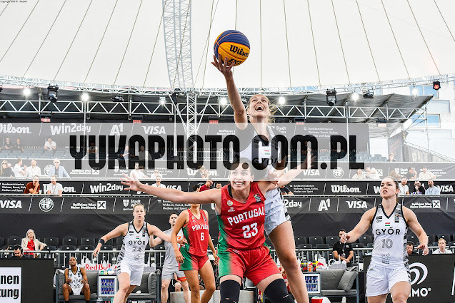 Dynamiczne ujęcie z meczu koszykówki 3x3. Zawodniczki w akcji, w tle trybuny i banery reklamowe. Widoczna piłka Wilson. Kadr pełen energii i sportowej rywalizacji.