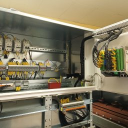 KOLBE - Otwarta szafa sterownicza z precyzyjnie ułożonymi przewodami oznaczonymi żółtymi etykietami, widoczne zabezpieczenia i listwy zaciskowe.