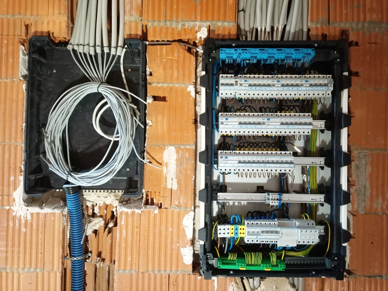 Rozdzielnia elektryczna w trakcie montażu w surowym murze. Widoczne kable, zabezpieczenia i elementy instalacji. Przewody ułożone w peszlach.