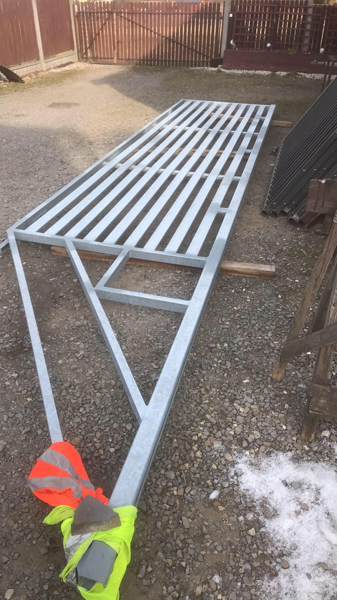 Szkielet metalowej konstrukcji bramy wjazdowej, z widocznymi spawami i elementami zabezpieczającymi, leżący na żwirowym podłożu w trakcie budowy.