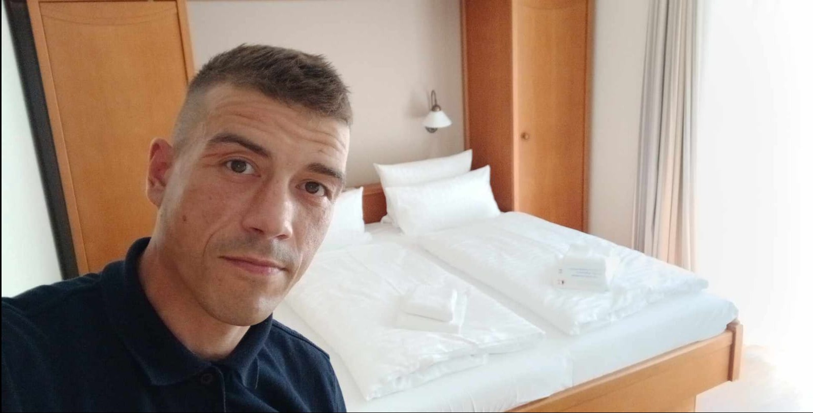 Wypoczęty mężczyzna na tle świeżo posłanego łóżka w Legnicy. Czysta pościel i schludne wnętrze sugerują profesjonalne przygotowanie pokoju.