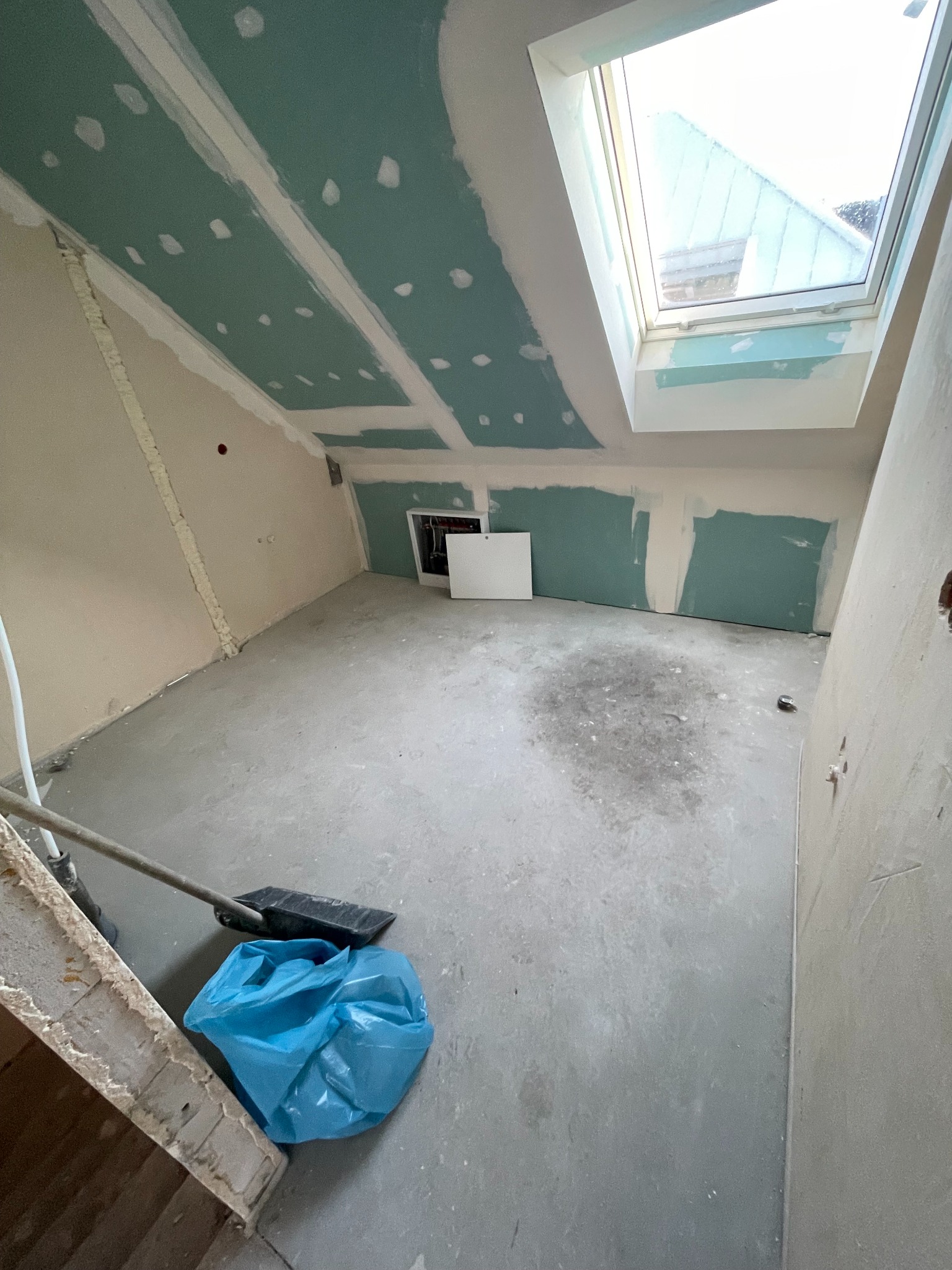 Poddasze w trakcie prac: płyty GK na skosach i suficie, widoczne łączenia. Okno dachowe, ślady po szpachlowaniu. Na podłodze śmieci i narzędzia.