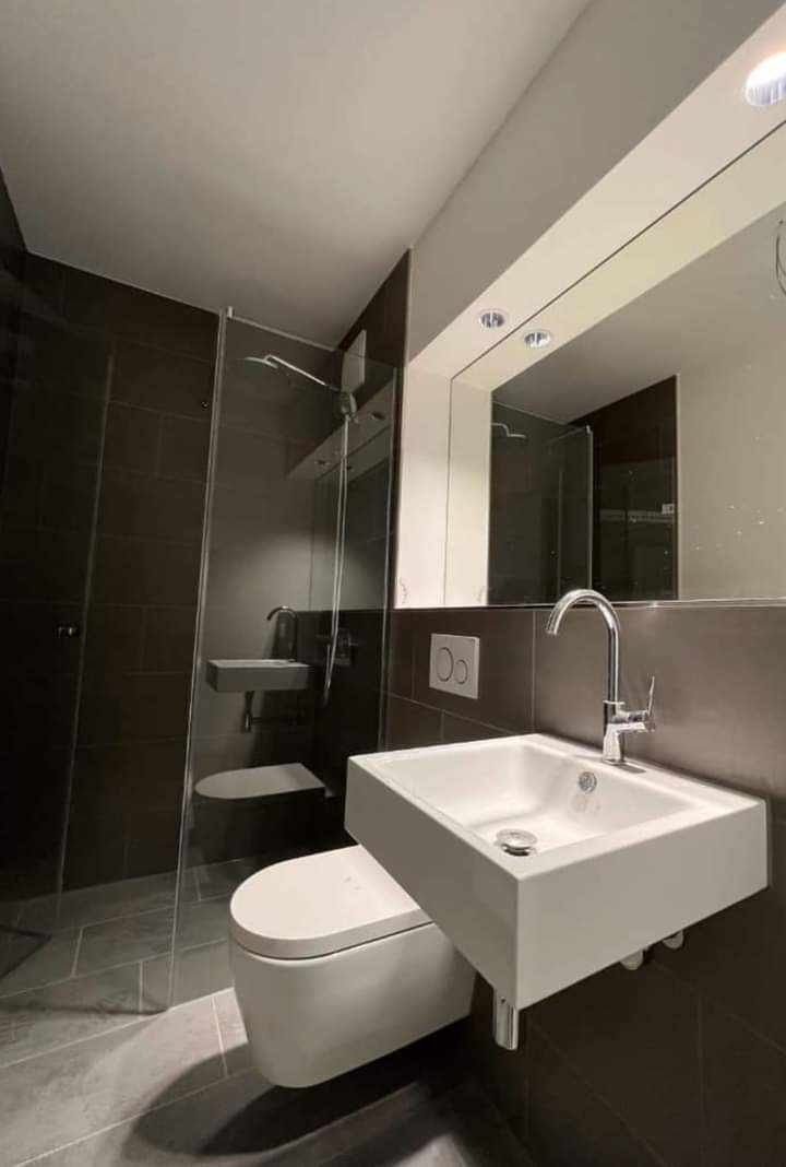 Nowoczesna łazienka w Zielonej Górze z kabiną prysznicową typu walk-in, podwieszaną toaletą i minimalistyczną umywalką nablatową na tle ciemnych płytek.