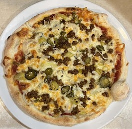 Apetyczna pizza z mięsem mielonym, cebulą i papryczkami jalapeno na białym talerzu, z dodatkiem czosnku. Idealna propozycja na catering firmowy.