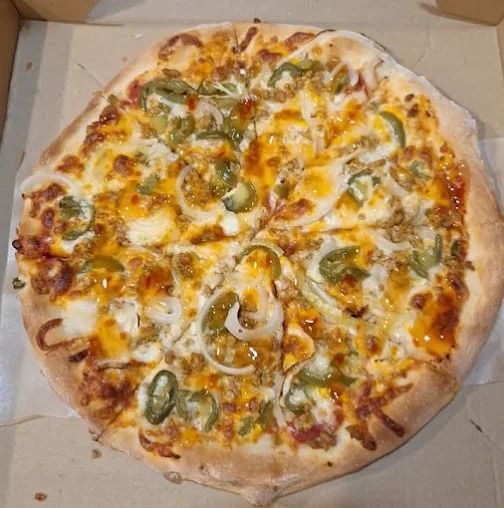 Pizza z jalapeno, cebulą i sosem, podana w kartonie. Widoczne plastry pizzy, gotowe do spożycia. Idealna na imprezę firmową lub spotkanie świąteczne.