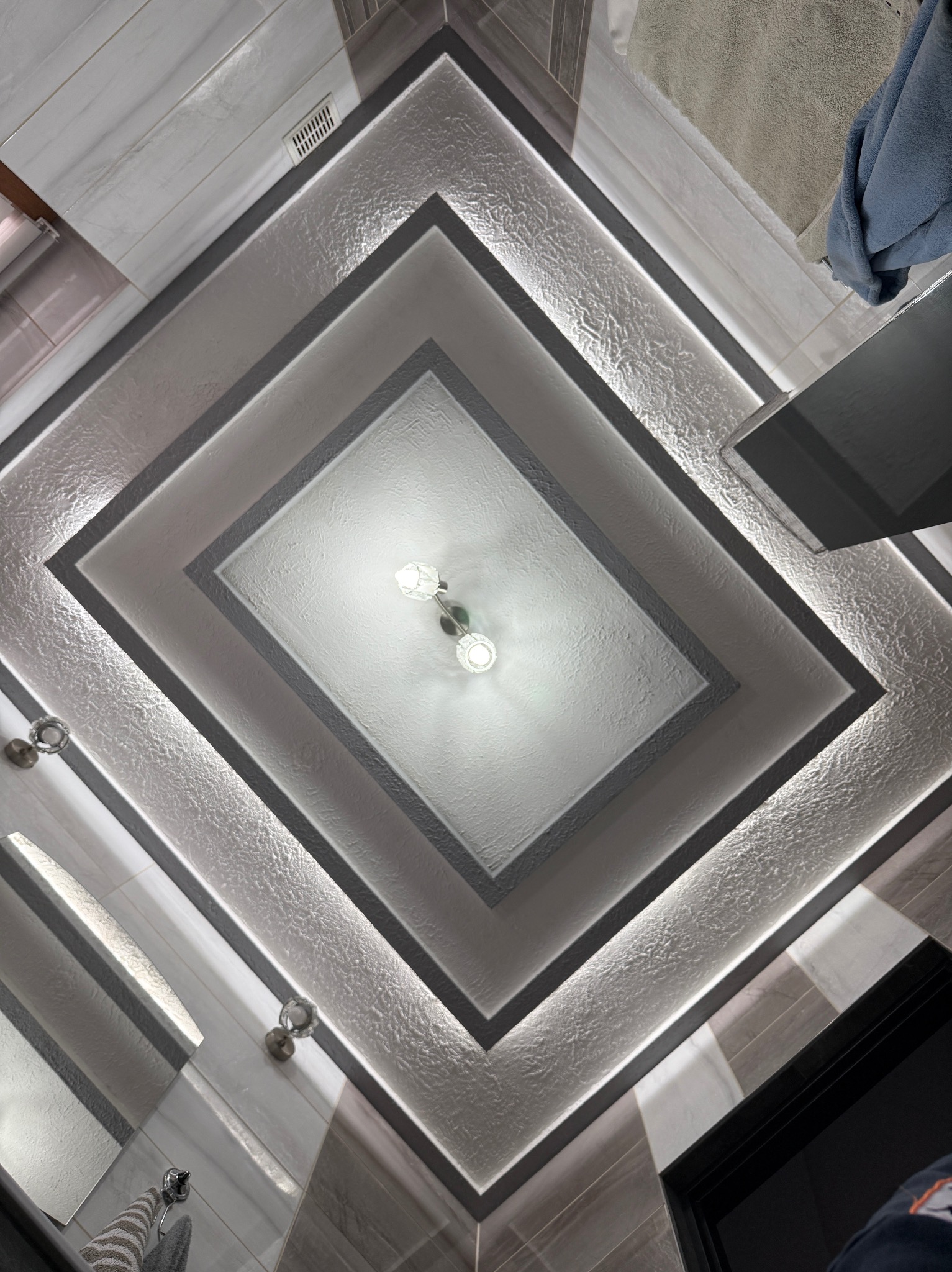 Geometryczny sufit w łazience z oświetleniem LED, ułożony w kwadraty. Widoczne płytki i lampy. Ujęcie z dołu, podkreślające detale wykończenia.