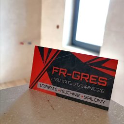 FR-GRES - Wizytówka firmy FR-GRES na tle wykończonej łazienki z oknem dachowym. Usługi glazurnicze: łazienki, kuchnie, salony. Czerwono-czarna grafika.