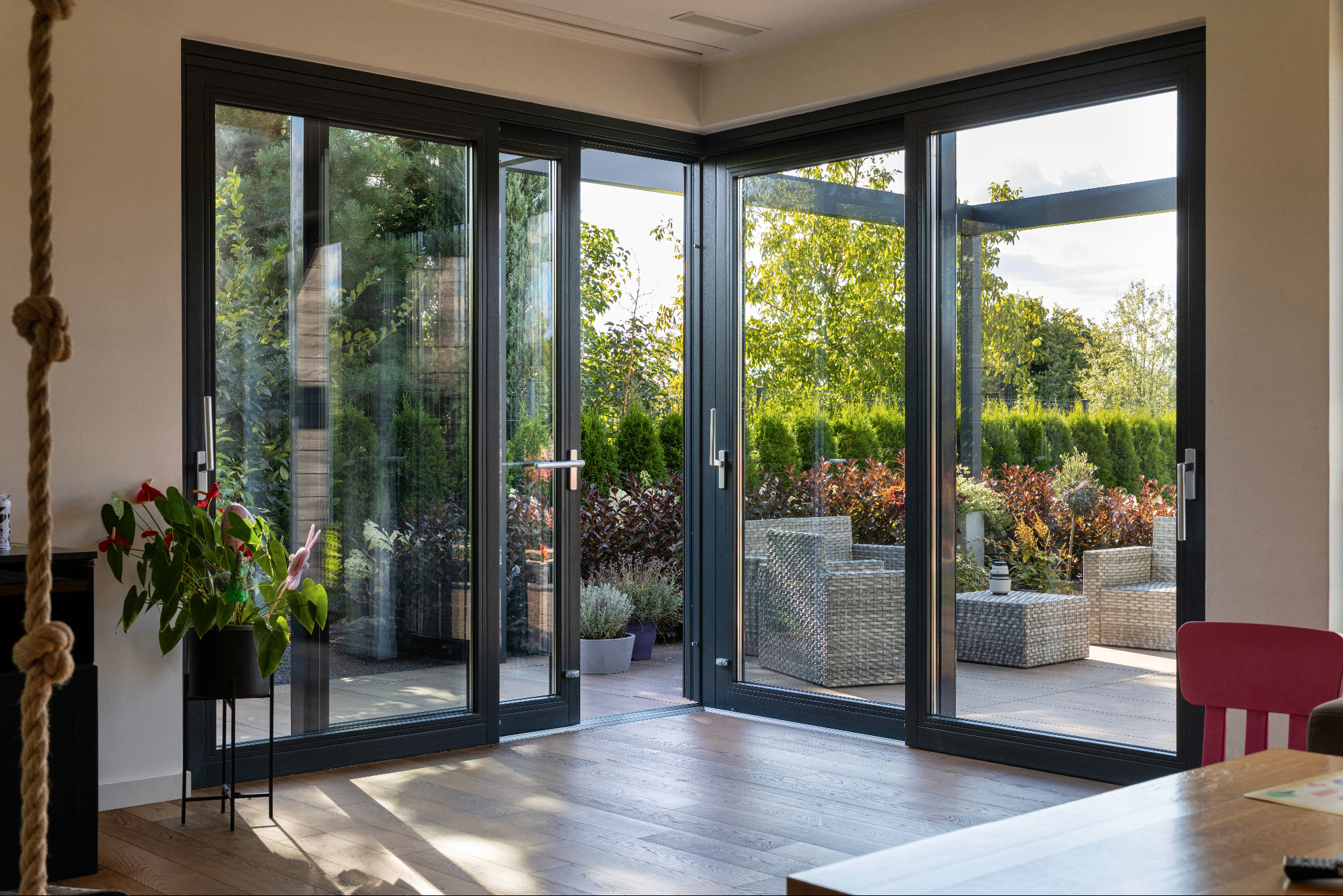 Nowoczesne, antracytowe drzwi przesuwne z widokiem na taras i ogród. Wnętrze doświetlone naturalnym światłem, drewniana podłoga, minimalistyczny design.