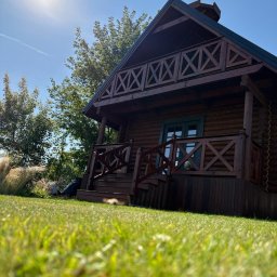 PYTON WOOD - Drewniany dom z balkonem w Bielsko-Białej, z charakterystycznymi zdobieniami w kształcie litery X. Ujęcie z poziomu trawy, słońce w górnym rogu kadru.