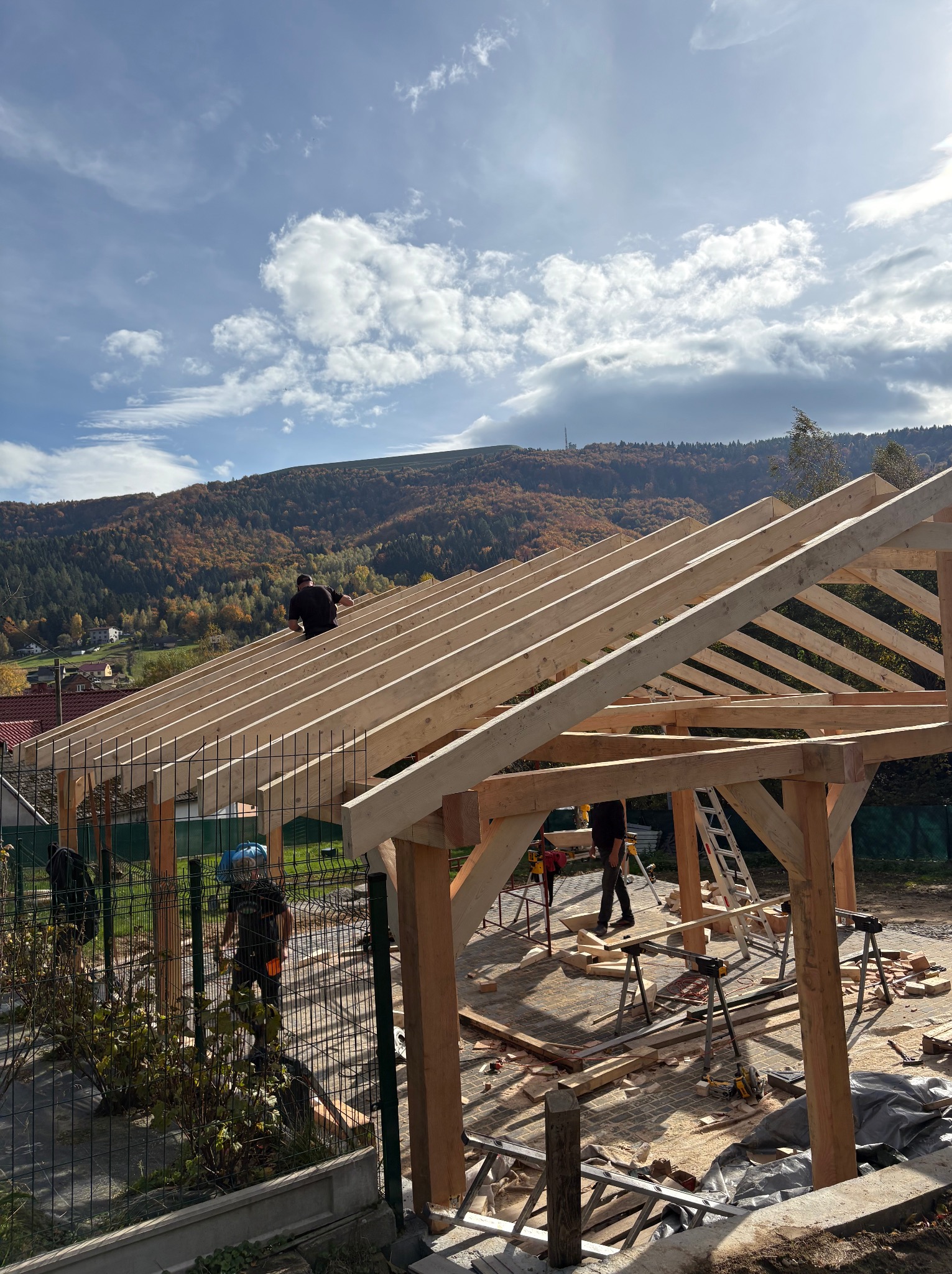 Montaż drewnianej konstrukcji dachu na tle górskiego krajobrazu. Widoczne elementy więźby i pracownicy podczas pracy na wysokości.