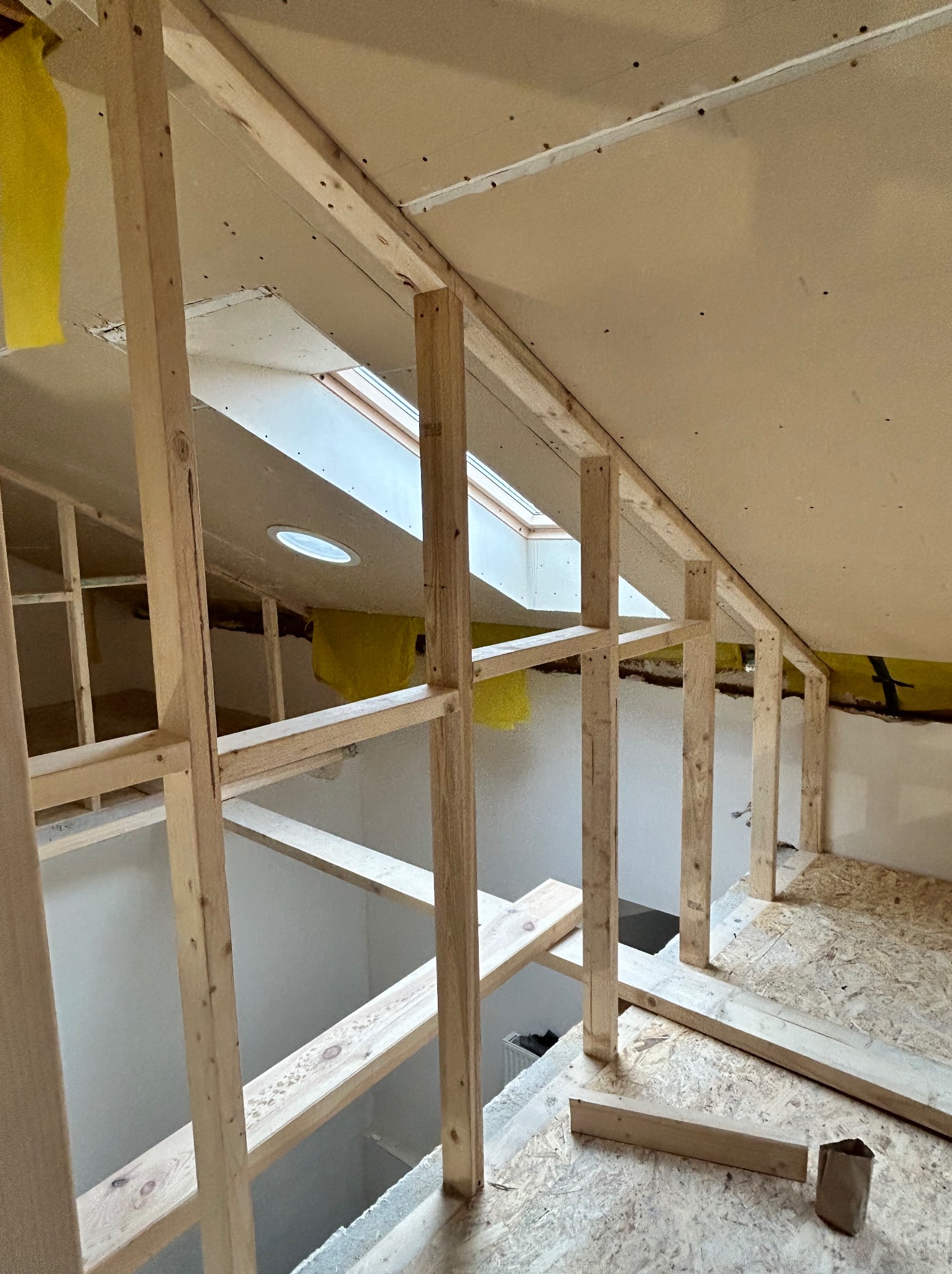 Wnętrze poddasza w trakcie adaptacji: drewniana konstrukcja szkieletowa, okno dachowe, izolacja z wełny mineralnej. Widoczne płyty gipsowo-kartonowe.