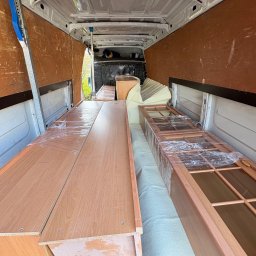 OMS Transport - Wnętrze furgonetki z zabezpieczonymi meblami (szafki, drzwi z szybami) owiniętymi folią stretch, gotowymi do transportu. Widoczne pasy mocujące.