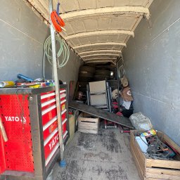 OMS Transport - Wnętrze busa wypełnione narzędziami, oponami i skrzyniami. Widoczny czerwony wózek narzędziowy YATO. Podłoga z widocznymi śladami użytkowania.