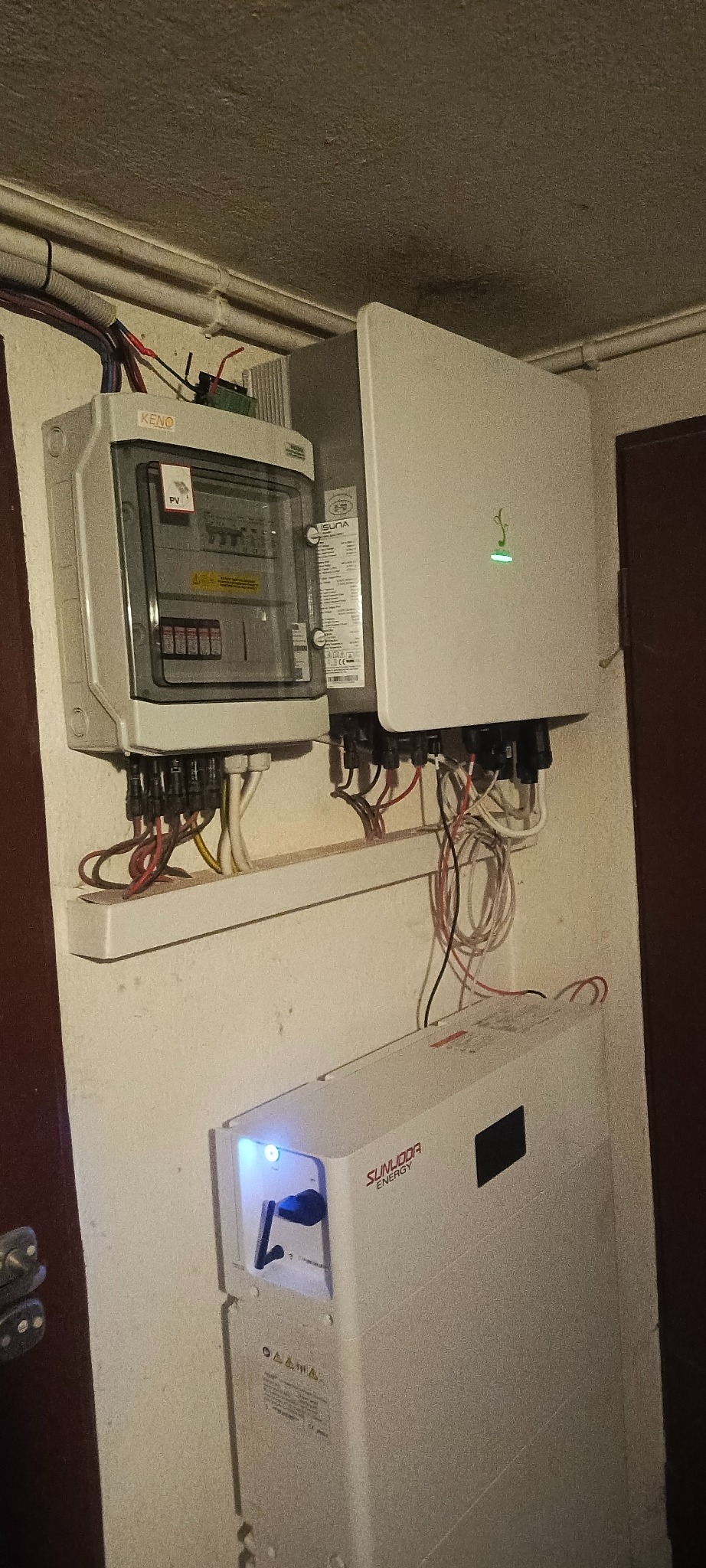 Zamontowany system fotowoltaiczny w pomieszczeniu: rozdzielnica Keno, inwerter Isuna i magazyn energii Sunooda. Widoczne przewody i elementy instalacji.
