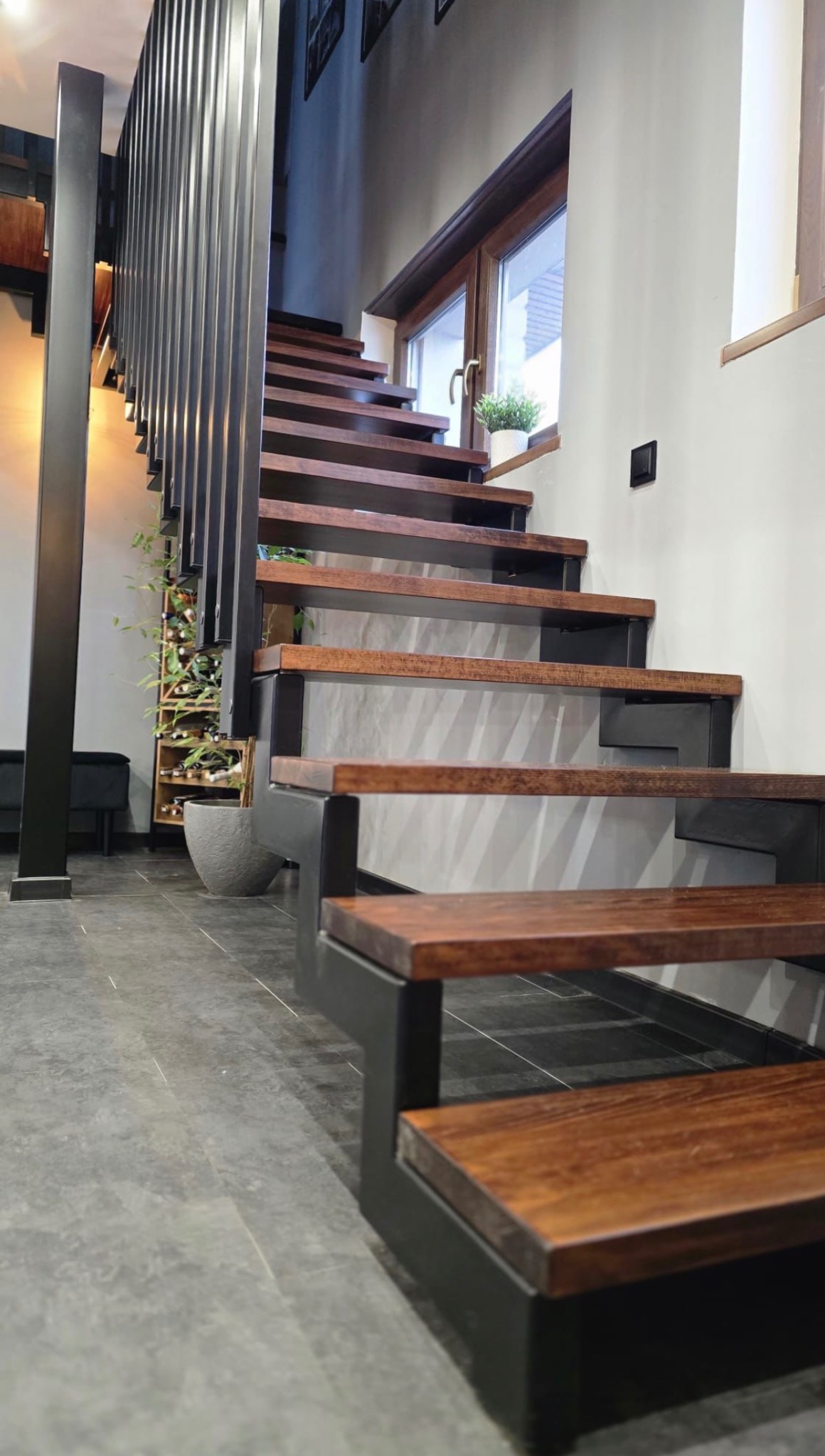 Nowoczesne schody drewniane z czarną metalową konstrukcją, widok z dołu, z elementami dekoracyjnymi w tle. Minimalistyczny design, naturalne światło.