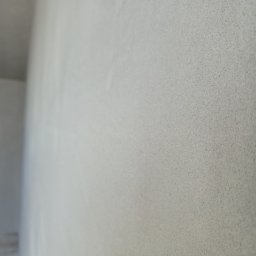 Perfekt Tynk - Świeżo nałożony, jasnoszary tynk na ścianie wewnętrznej, widoczna delikatna faktura i gładka powierzchnia. Minimalistyczne ujęcie z bliska.