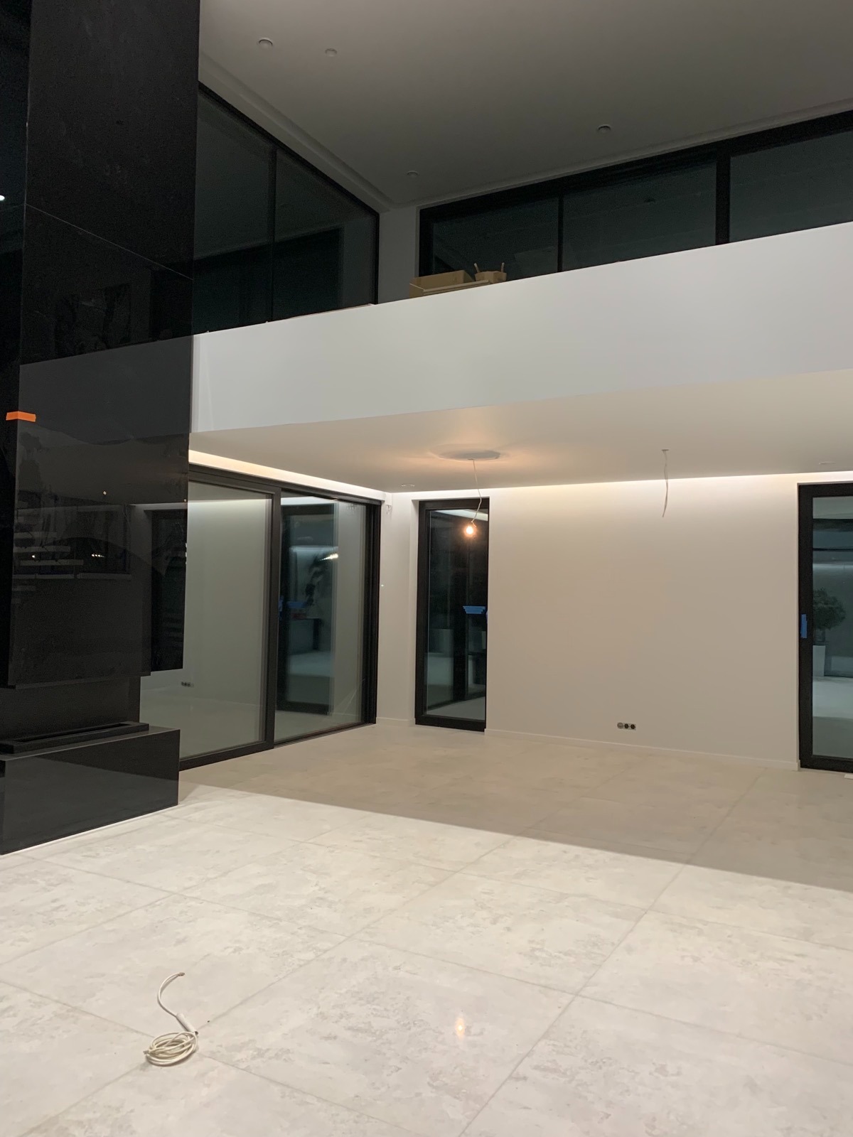 Nowoczesne wnętrze z jasną podłogą, dużymi oknami i czarnym elementem dekoracyjnym. Minimalistyczny design, świeżo po wykończeniu, z widocznymi detalami instalacji.