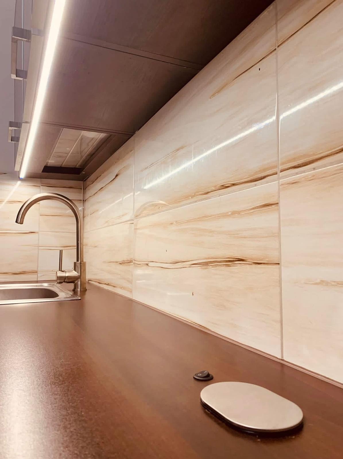 Kuchnia po remoncie: brązowy blat, beżowe płytki z wzorem, chromowana bateria i podświetlenie LED pod szafkami, tworzące ciepłą atmosferę.