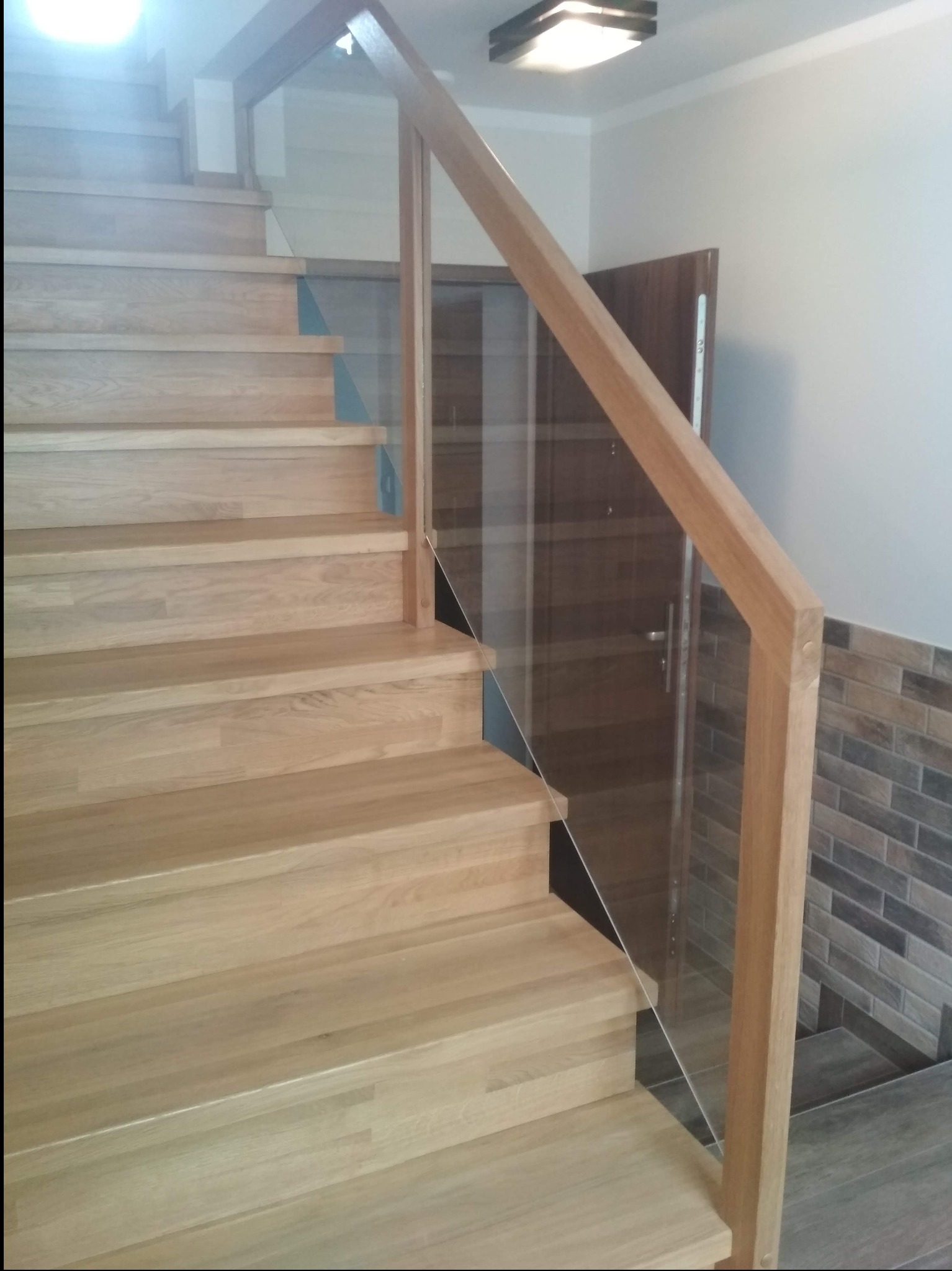 Jasne schody drewniane z balustradą ze szkła i drewna, widoczne z dołu. Ujęcie podkreśla naturalne wykończenie drewna i minimalistyczny design balustrady.