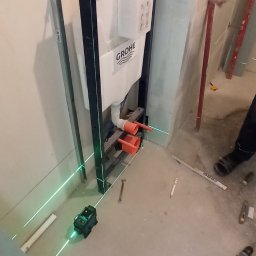 Oleg Andronik AndroBud - Montaż stelaża podtynkowego Grohe we Wrocławiu, widoczne narzędzia i laser krzyżowy. Prace instalacyjne w łazience, przygotowanie do wykończenia.