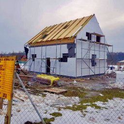 Steelvio House - Budowa domu w technologii szkieletowej w zimowej scenerii. Widoczne rusztowania, tablica informacyjna i elementy konstrukcyjne dachu. Prace w toku.