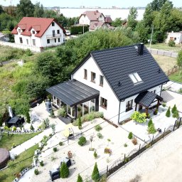Steelvio House - Nowoczesny dom szkieletowy z ciemną dachówką i jasną elewacją, widok z góry. Uwagę zwraca zagospodarowany ogród z jacuzzi i meblami ogrodowymi.