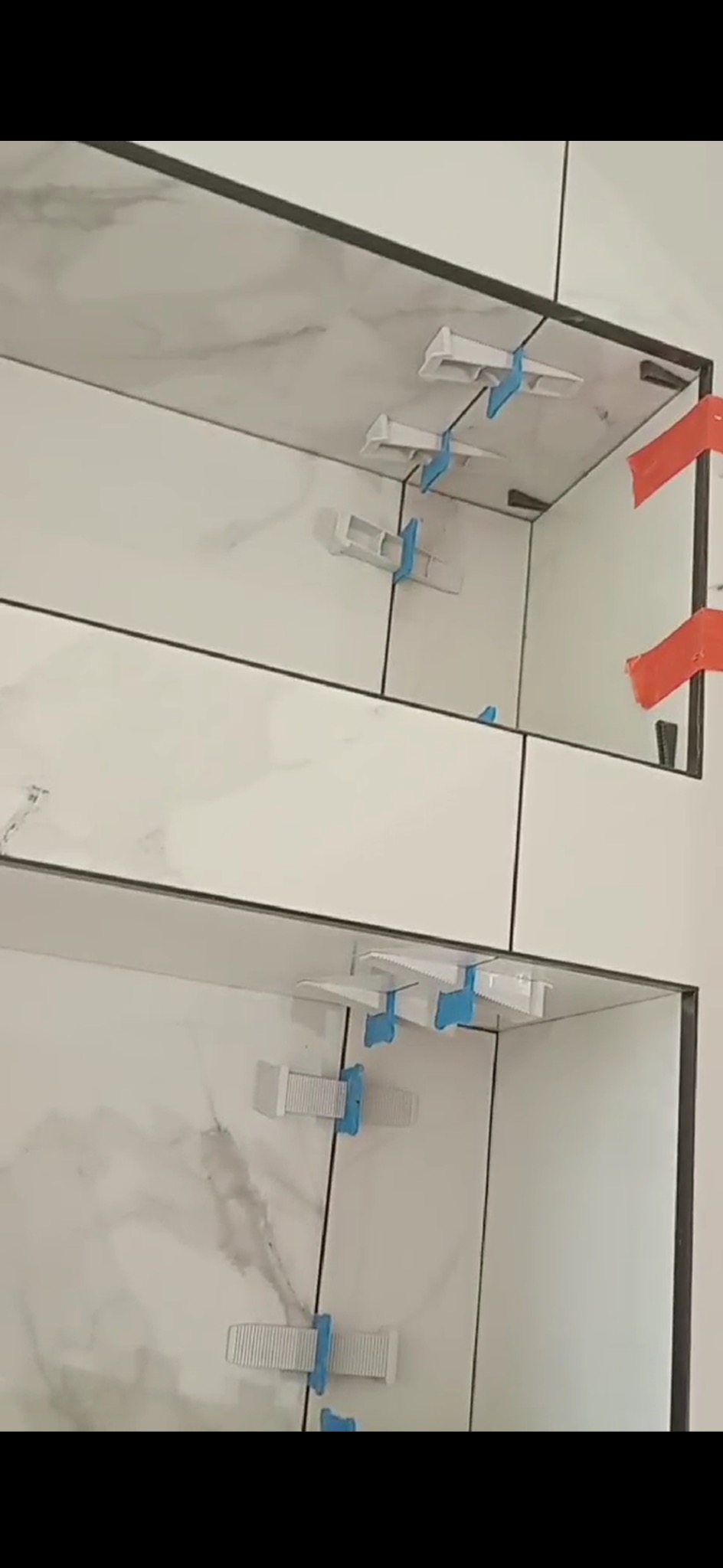 Białe płytki imitujące marmur, ułożone z użyciem klipsów poziomujących i krzyżyków dystansowych, czarne fugi, widok z bliska.