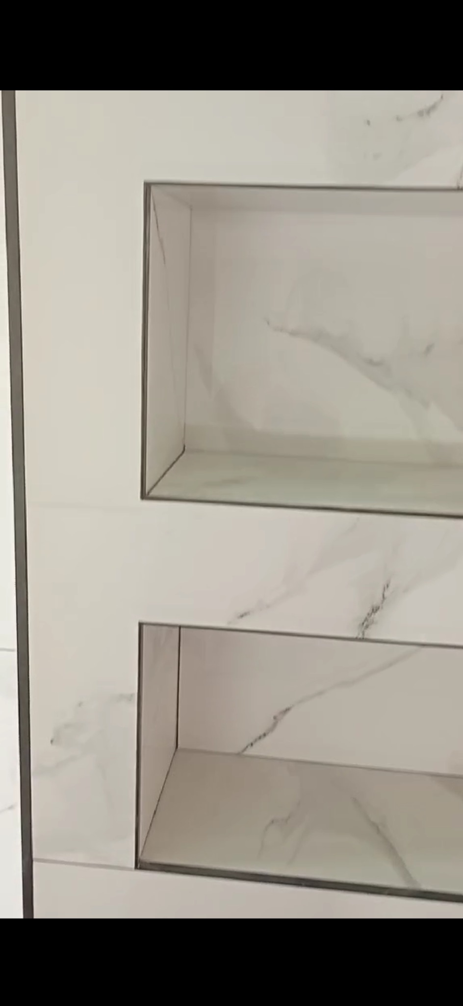 Białe płytki imitujące marmur z wnękami wykończonymi szarą listwą. Minimalistyczny design łazienki, nowoczesne wykończenie ściany z półkami.