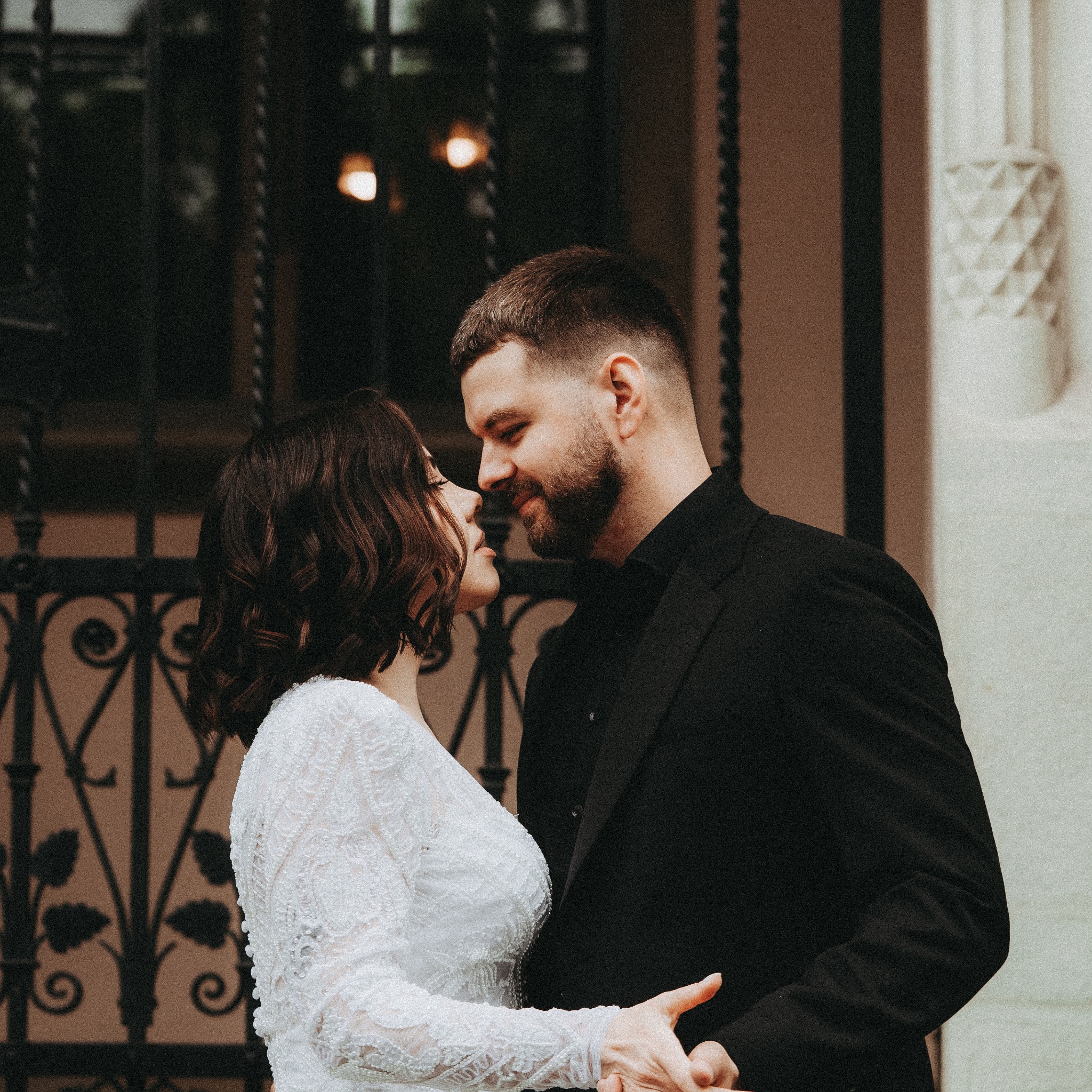 Para młoda w zbliżeniu, panna młoda w koronkowej sukni, pan młody w czarnym garniturze, romantyczny kadr na tle ozdobnej bramy.