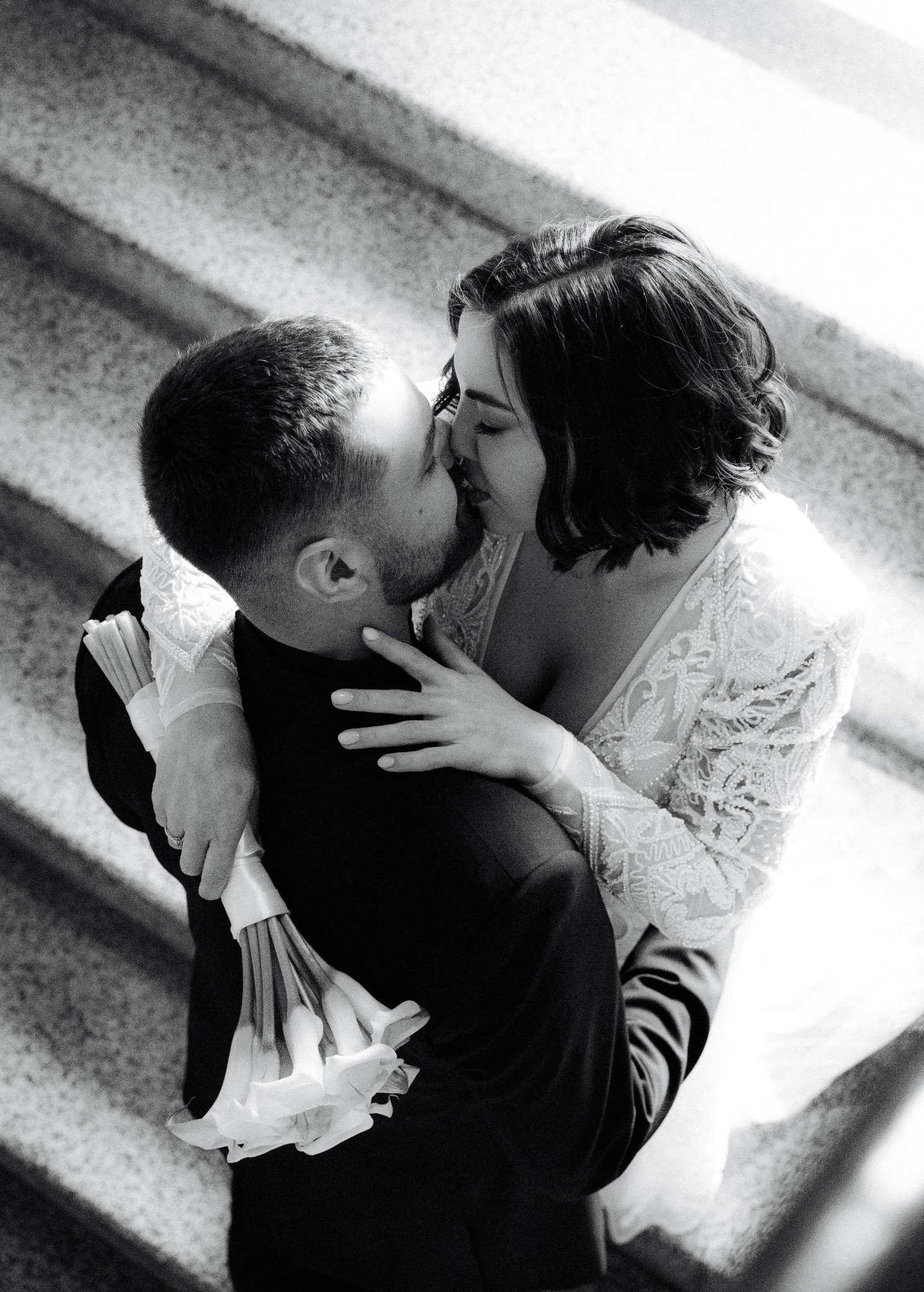 Czarno-białe zdjęcie całującej się pary młodej na schodach w Krakowie. Panna młoda w koronkowej sukni trzyma bukiet.