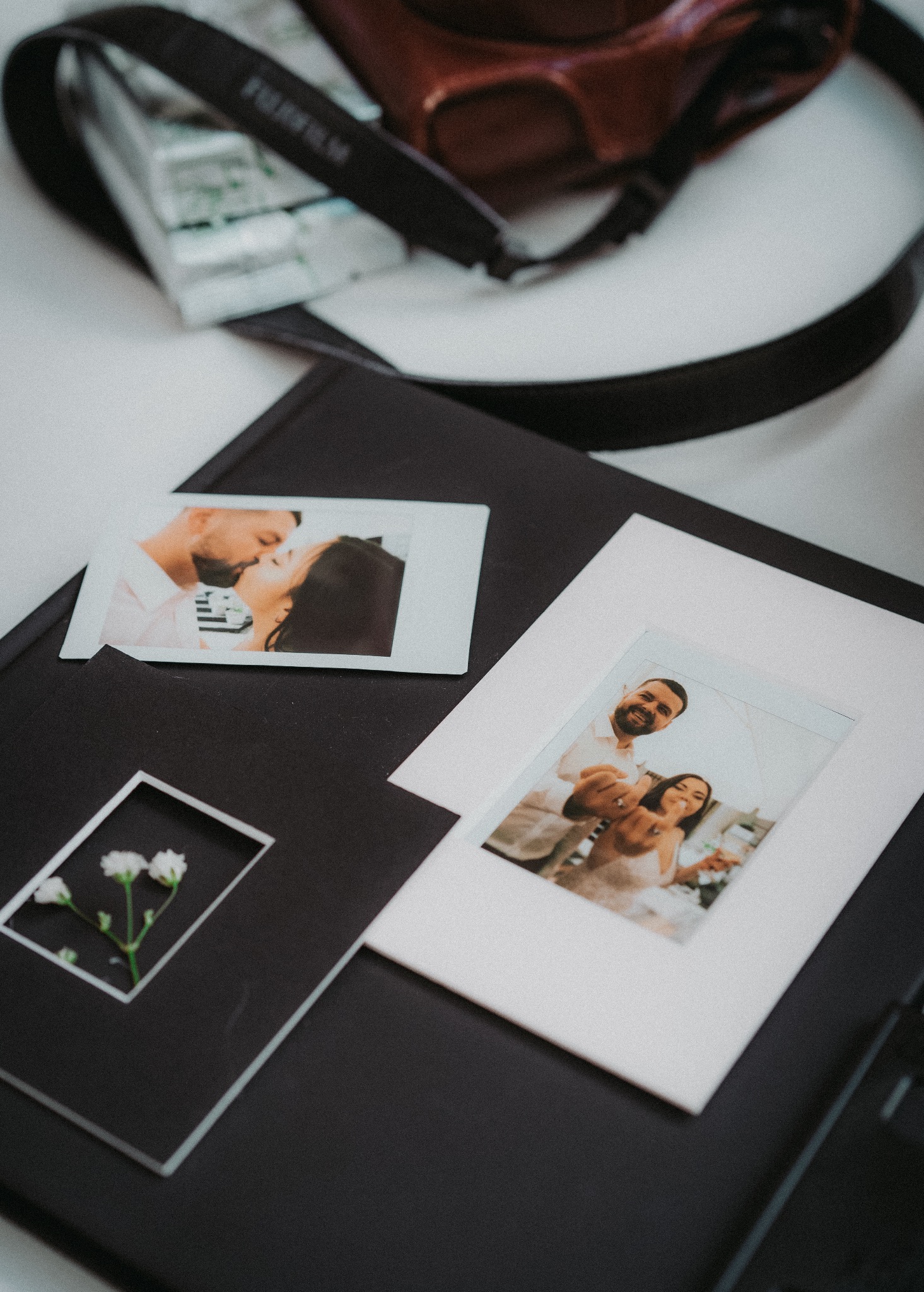 Album ślubny z polaroidowymi zdjęciami pary, kwiaty w ramce, aparat Fujifilm w tle. Pamiątka z uroczystości, uchwycone emocje, detale.