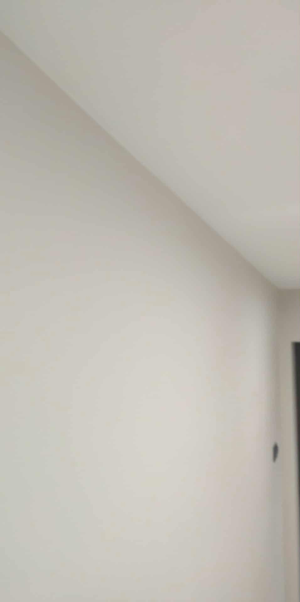 Gładka, beżowa ściana po malowaniu, widoczny fragment sufitu i krawędź drzwi. Minimalistyczne wnętrze, jednolite wykończenie.