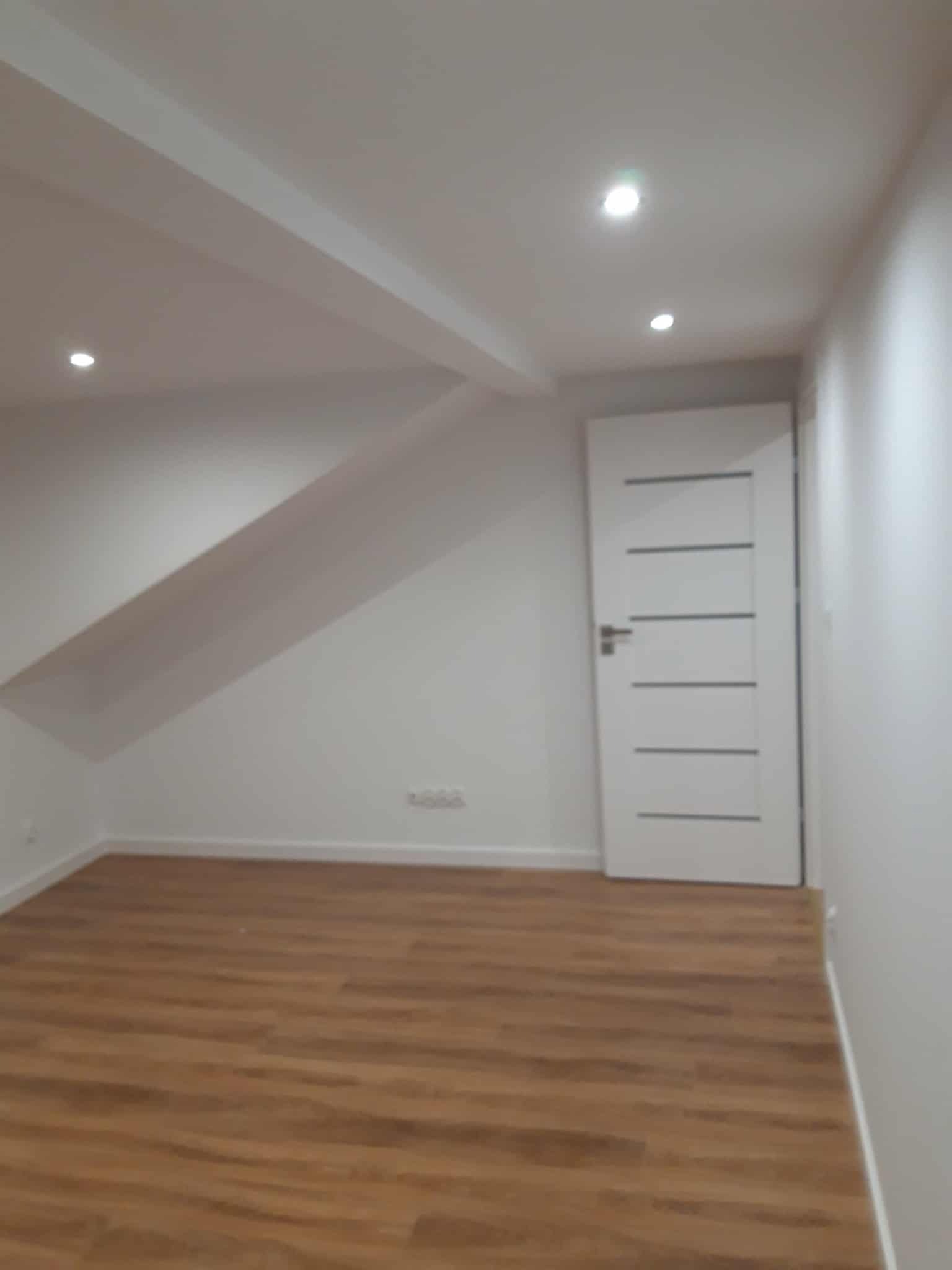 Jasne wnętrze po remoncie: drewnopodobne panele, białe ściany i drzwi z poziomymi frezami. Oświetlenie punktowe w suficie.