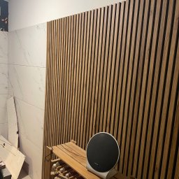 Oleksandr Potapchuk - Drewniane lamele na ścianie w trakcie montażu, widoczne narzędzia i fragment ściany z marmurowymi płytkami. Częściowo wykończone wnętrze.