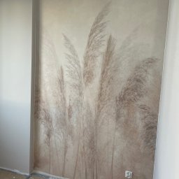 Oleksandr Potapchuk - Ściana z dekoracyjną tapetą w odcieniach beżu, przedstawiającą motyw trawy pampasowej. Widoczny fragment podłogi w trakcie prac wykończeniowych i gniazdko elektryczne.