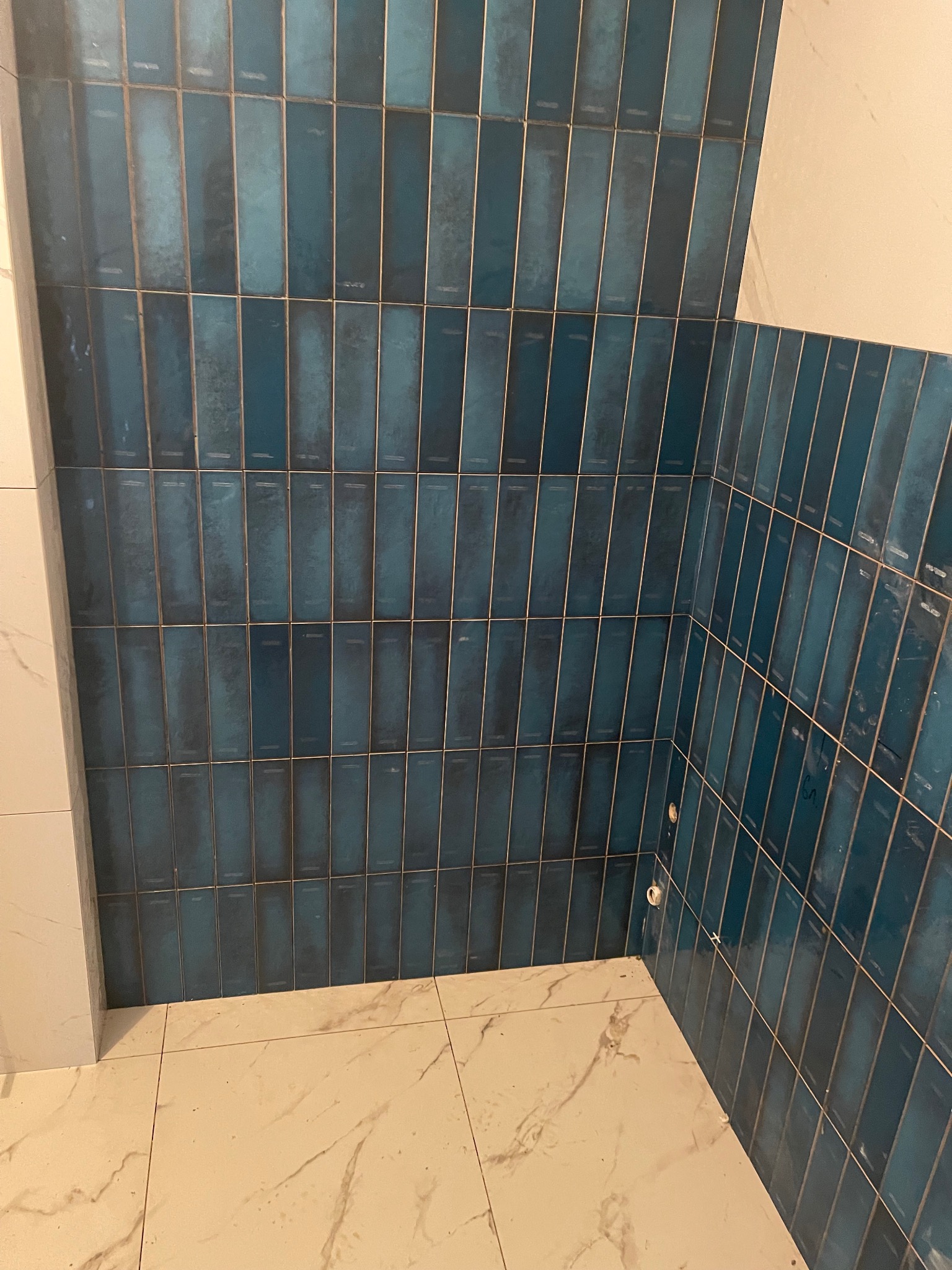 Ukończona łazienka z pionowo ułożonymi, błyszczącymi, turkusowymi płytkami na ścianach i marmurową podłogą. Widoczne detale wykończenia.